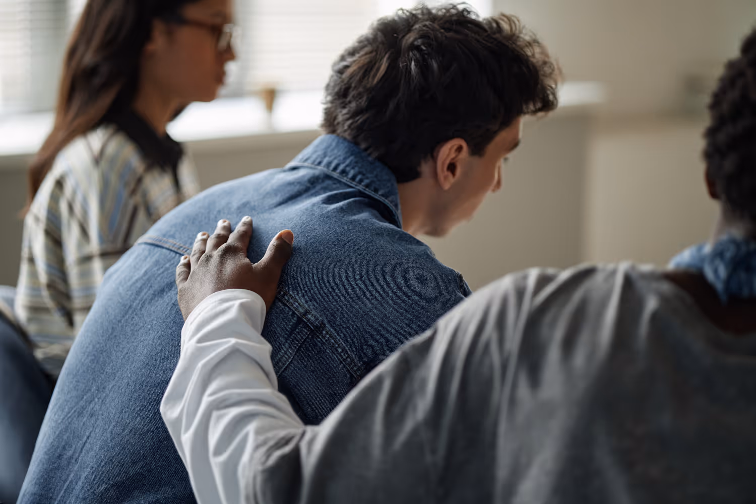 Kind im Zentrum GbR – Beratung – Gruppe Jugendlicher unterschiedlicher Herkunft nimmt an einer Beratungssitzung teil. Ein schwarzer Jugendlicher legt einem weißen Jugendlichen sanft die Hand auf den Rücken. Teenager